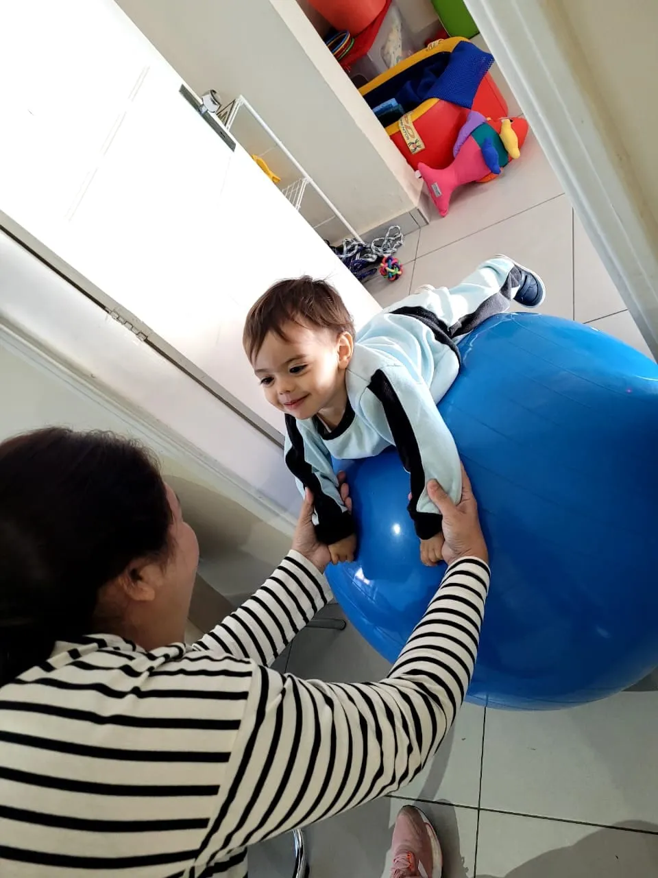 Criança sendo apoiada sobre uma bola terapêutica azul