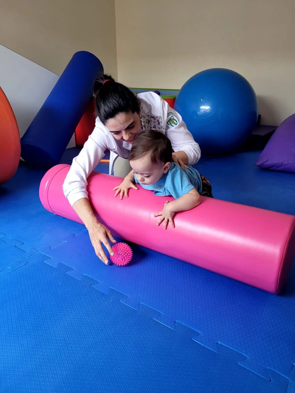 Terapeuta ajudando criança a atravessar um rolo terapêutico rosa