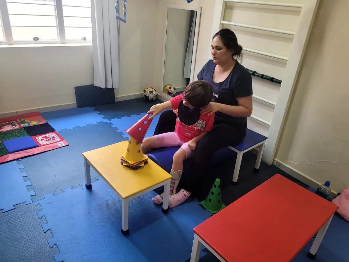 Terapeuta ajustando a postura de uma criança sentada em uma cadeira adaptada