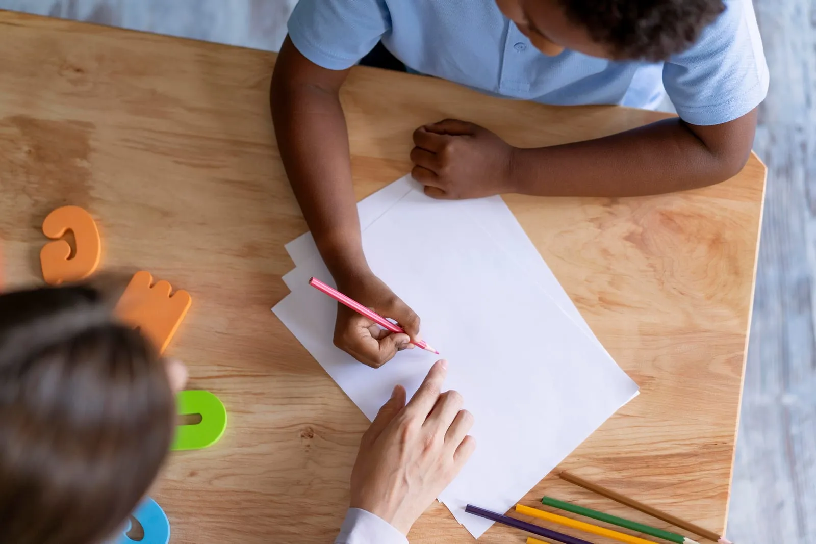 Mãos de uma criança desenhando em uma folha de papel com apoio de uma adulta