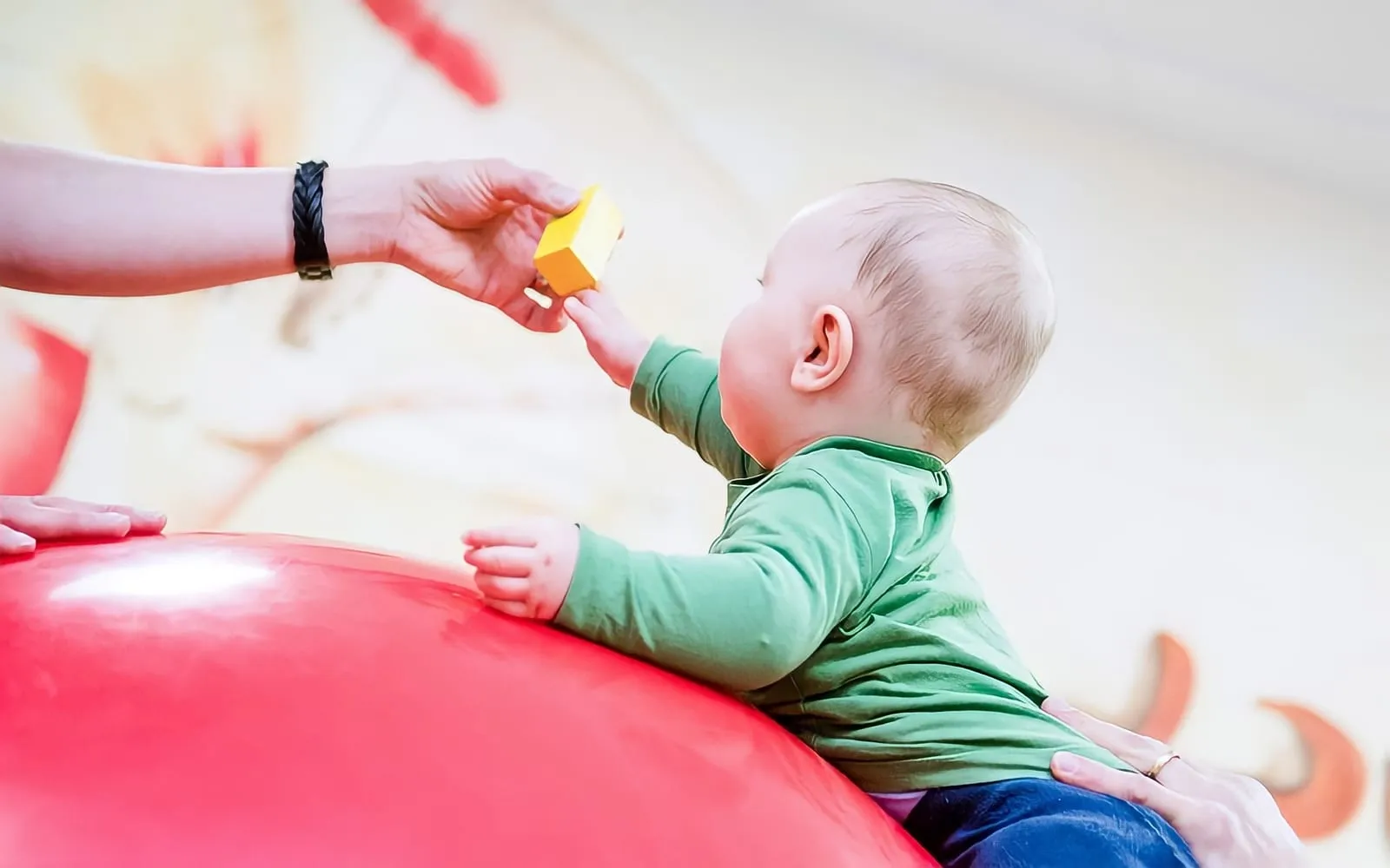 Terapeuta oferecendo um brinquedo a um bebê apoiado sobre uma bola terapêutica